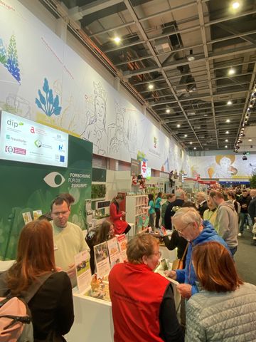 Das Bild zeigt mehrere sich im Gespräch befindende Personen an einem Messestand in einer großen Halle.