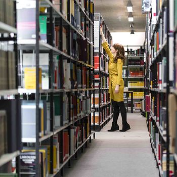 Bibliothek Frau am Bücherregal Thema Promotion an KAT-Hochschulen