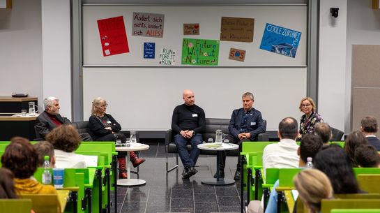 Fünf Menschen sitzen nebeneinander, hinter ihnen hängen Plakate mit Klimaprotestsprüchen.
