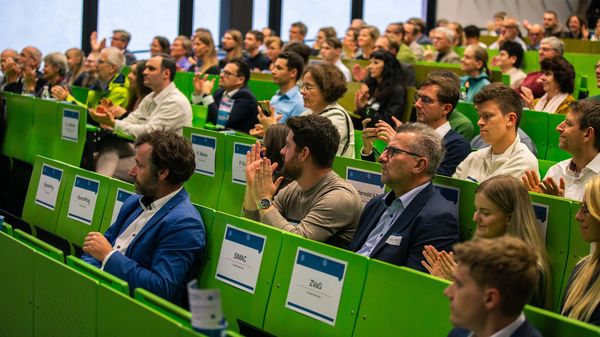 In einem Hörsaal einer Hochschule sitzen sehr viele Menschen. Sie applaudieren.