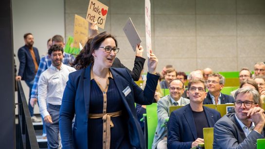 Fünf Personen laufen mit Plakaten in der Hand am sitzenden Publikum vorbei.