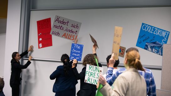Eine Handvoll Personen hält Plakate mit Slogans für den Klimaschutz in der Hand. Sie laufen auf die Bühne und demonstrieren.