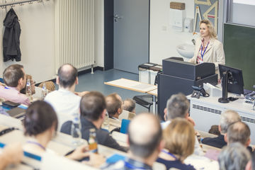 Zu sehen ist eine Frau, die hinter einem Pult stehend eine Rede hält.