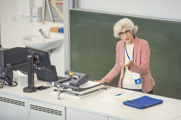 Zu sehen ist eine Frau hinter einem Pult, die gestikulierend eine Rede hält.