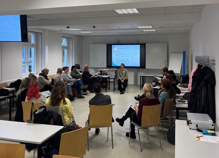 Zu sehen ist ein Konferenzraum, in dem mehrere Personen auf im Kreis angeordneten Stühlen sitzen und miteinander diskutieren.