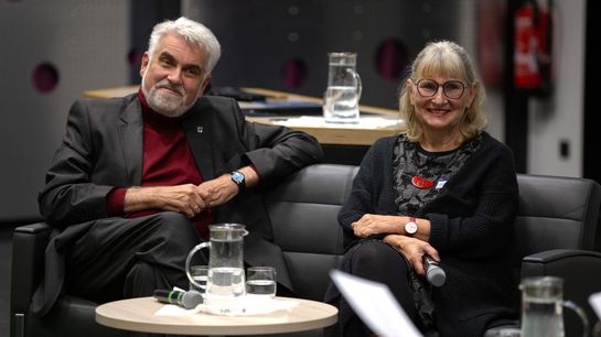 Ein Mann und eine Frau sitzen, freundlich guckend, auf einem Sofa.
